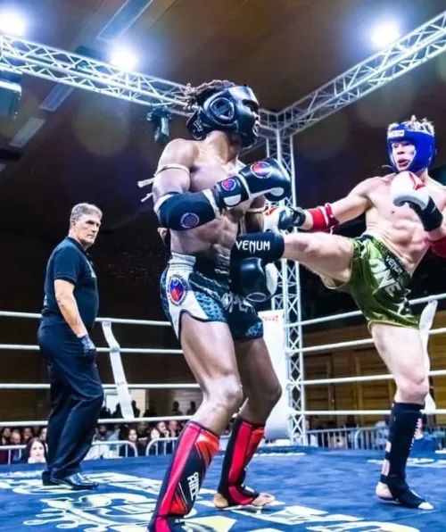 Combat intense de Muay Thai. Un athlète bloque un coup de pied puissant lors d'un affrontement technique en boxe thaï. L'entraînement rigoureux en club permet de perfectionner la défense et la contre-attaque.